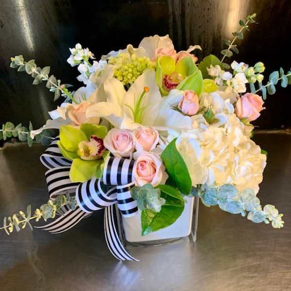 White and pink floral arrangement in a square vase with a striped ribbon