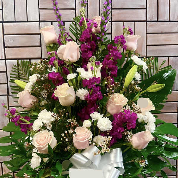 Pink roses and purple flowers arranged in a vase with a white ribbon