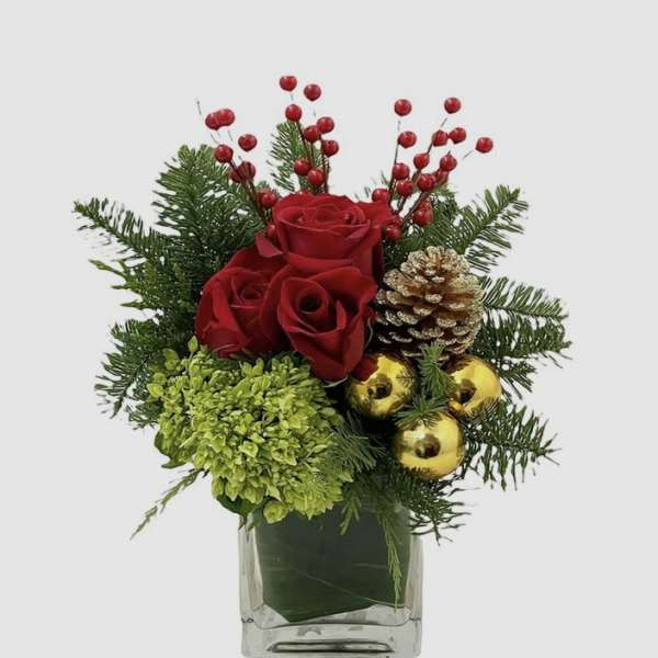 Red roses with pine, berries, and gold ornaments in a glass vase