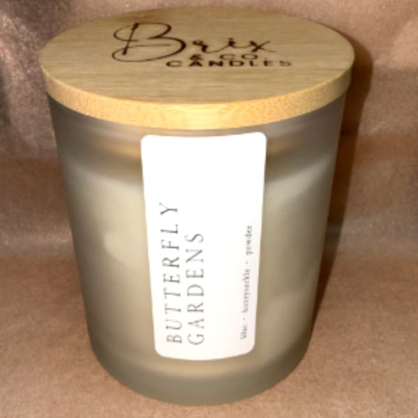 Frosted glass candle jar with a wooden lid labeled Butterfly Gardens