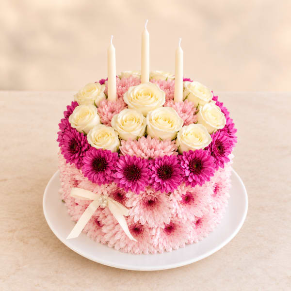 Round floral cake with white roses, pink daisies, and three white candles