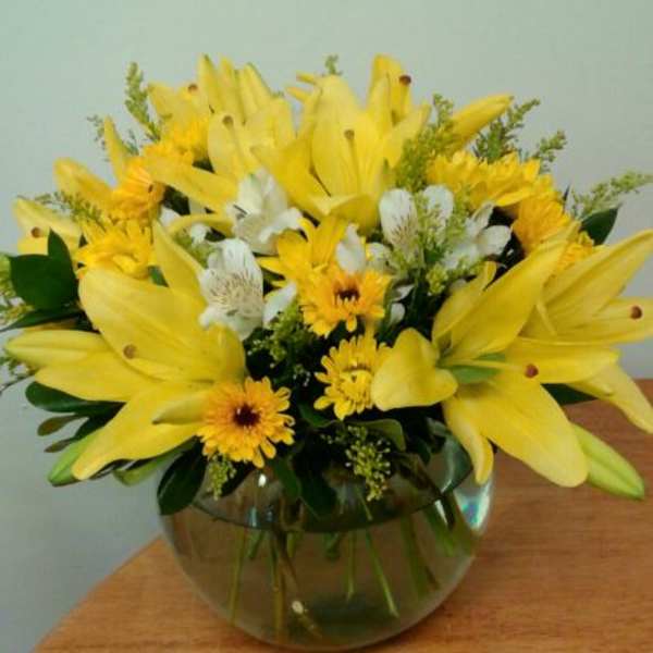 Yellow lilies and daisies in a round glass vase