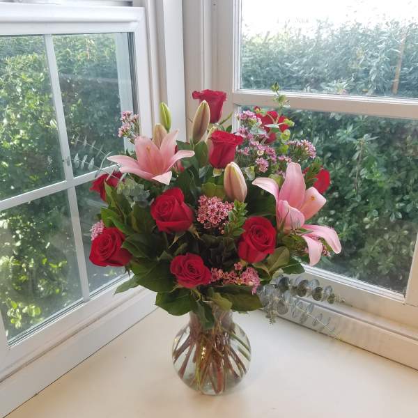 Pink lilies and red roses arranged in a clear glass vase