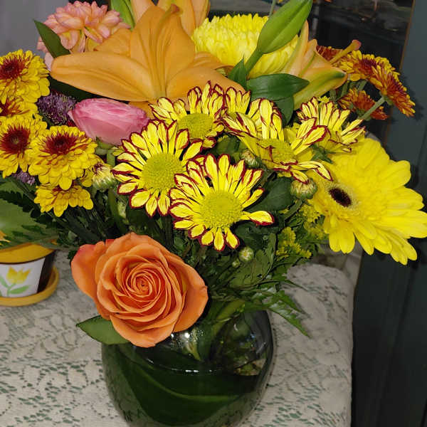 Mixed bouquet with orange roses, yellow lilies, and chrysanthemums in a glass vase