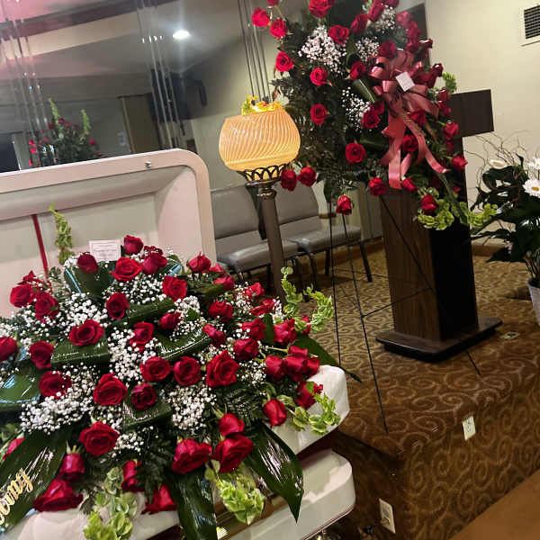 Large red rose funeral spray on a casket with a matching standing spray