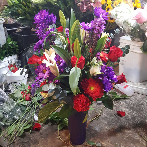Mixed bouquet with red roses, purple flowers, and white lilies in a tall vase