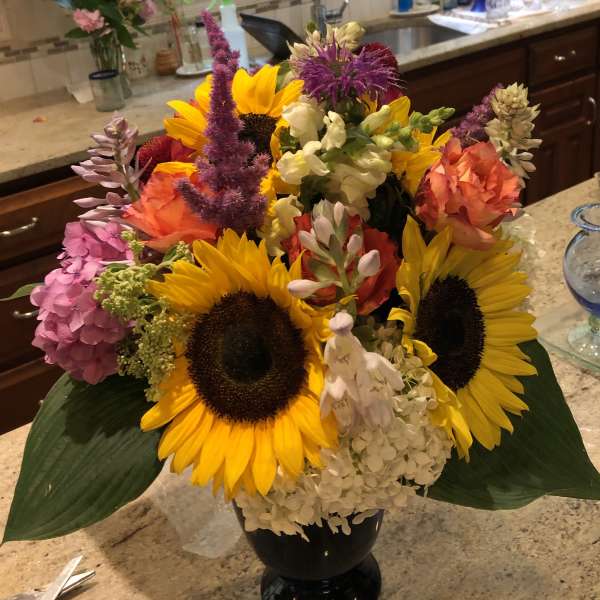 Colorful bouquet with sunflowers, hydrangeas, and snapdragons in a black vase