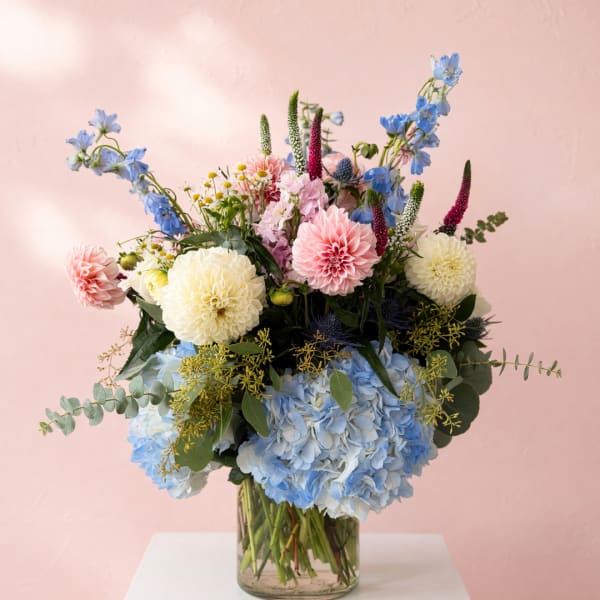 Mixed pastel bouquet in a clear glass vase with blue hydrangeas and pink dahlias