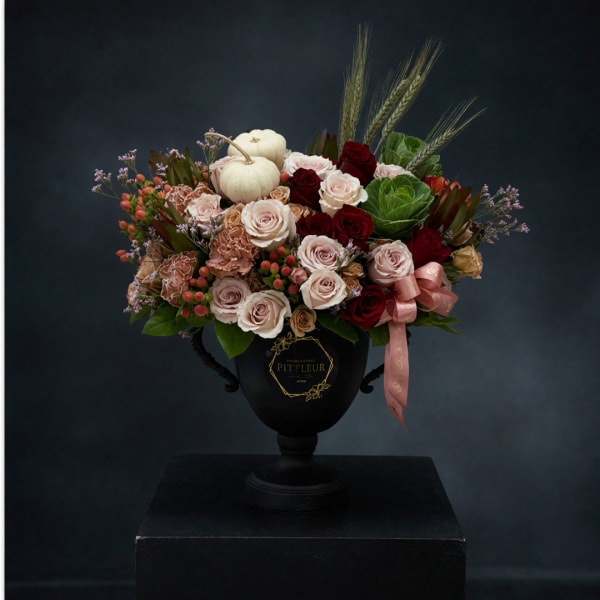 Mixed rose arrangement in a black urn with white pumpkins and a pink ribbon