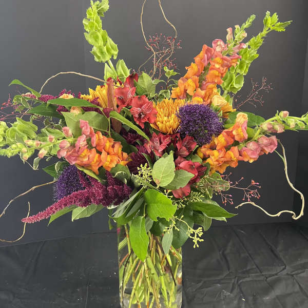 Colorful mixed bouquet in a clear glass vase with orange, pink, purple, and yellow blooms