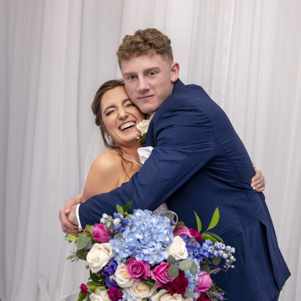 Bride and groom hugging with a colorful wedding bouquet in front