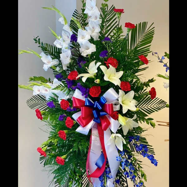 Tall standing floral spray with white lilies, red carnations, and blue ribbon