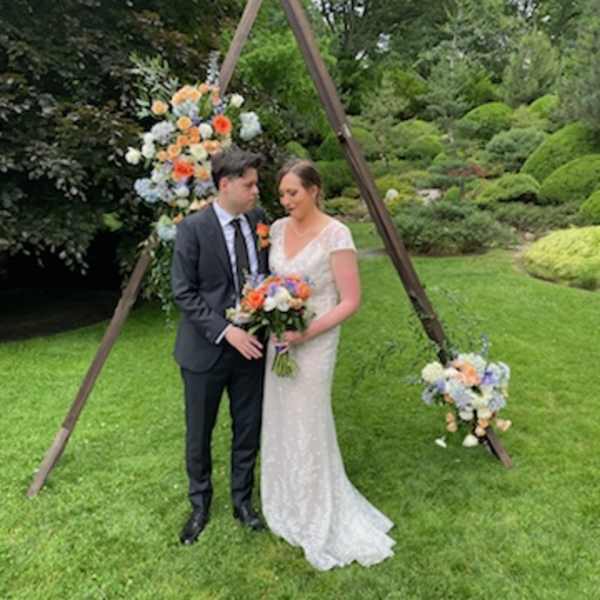 Bride and groom with colorful wedding flowers under a wooden arch