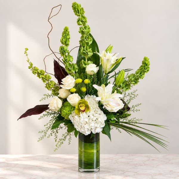 Tall white and green floral arrangement in a glass vase