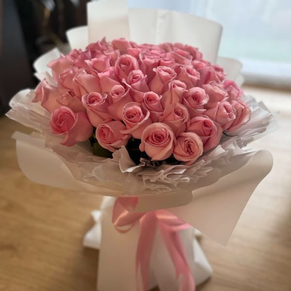 Bouquet of pink roses wrapped in white paper with a pink ribbon