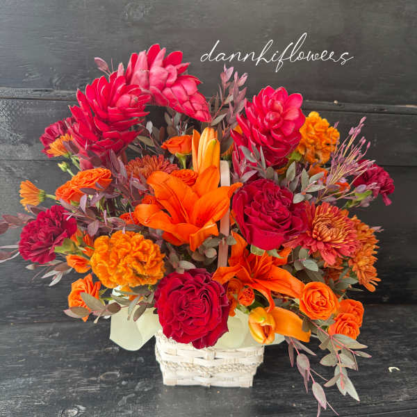 Bright orange and red floral arrangement in a white basket
