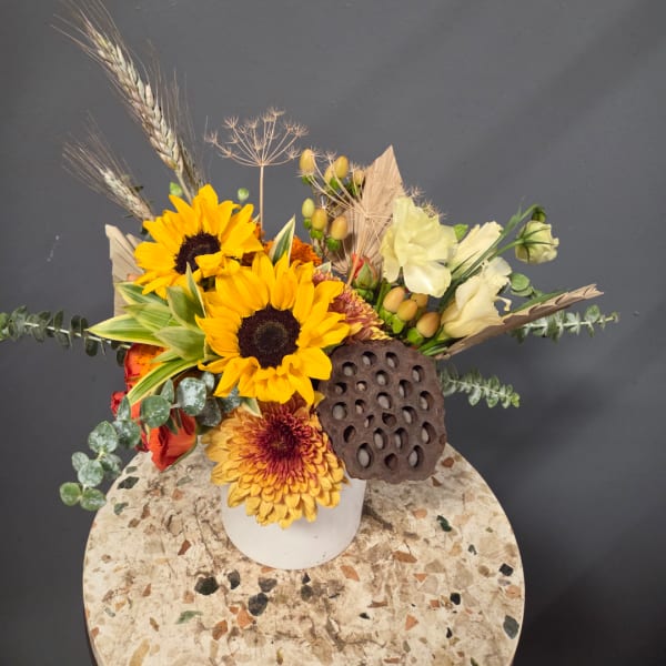 Sunflower arrangement in a white vase with pale blooms and dried accents
