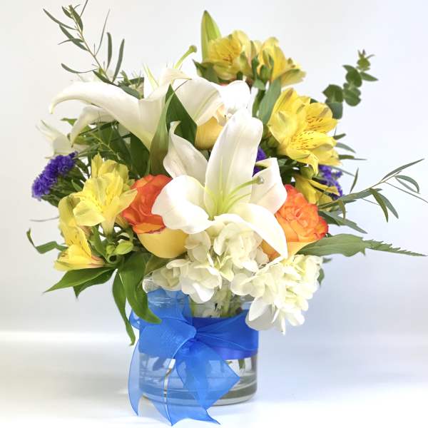 Bouquet of white lilies, yellow alstroemeria, and orange roses in a glass vase
