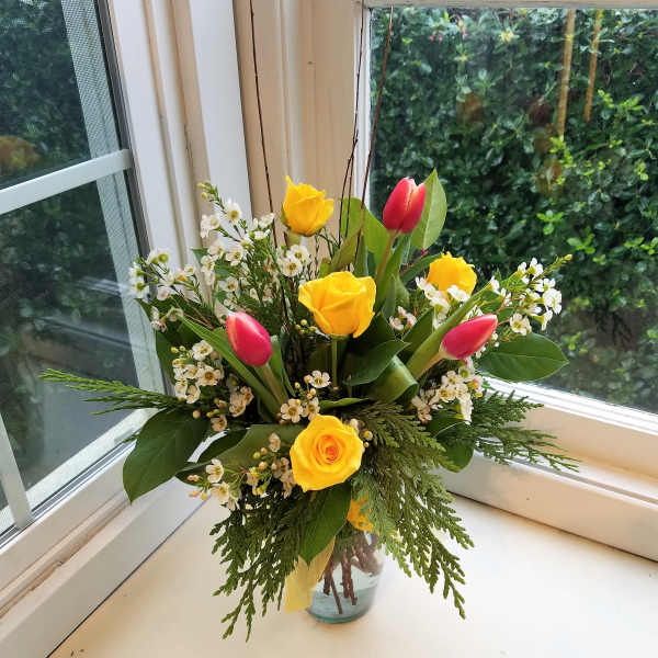 Yellow roses and pink tulips in a glass vase with white filler flowers