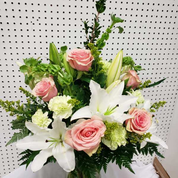 Pink roses and white lilies in a glass vase with green accents