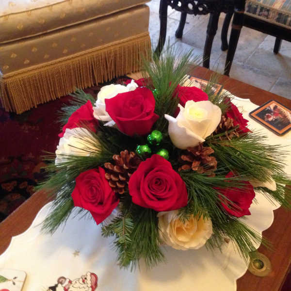 Red and white roses arranged with pine and pinecones in a low centerpiece