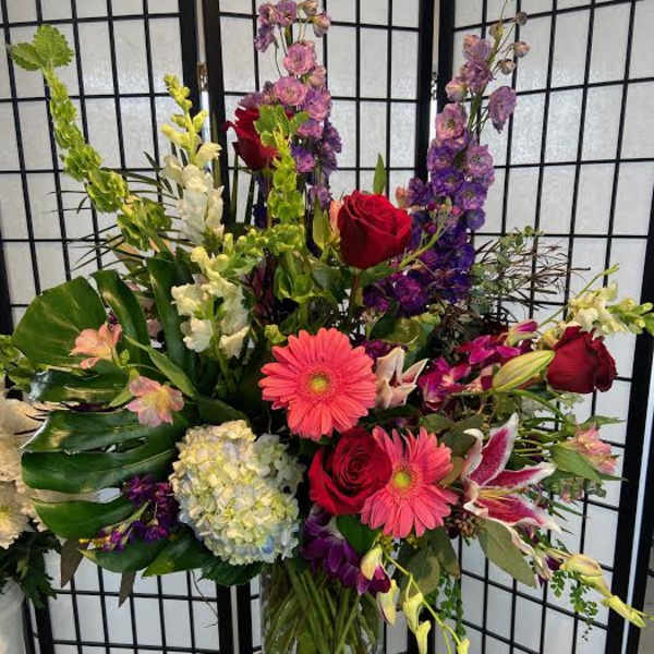 Mixed bouquet in a glass vase with red roses, pink gerberas, and purple flowers