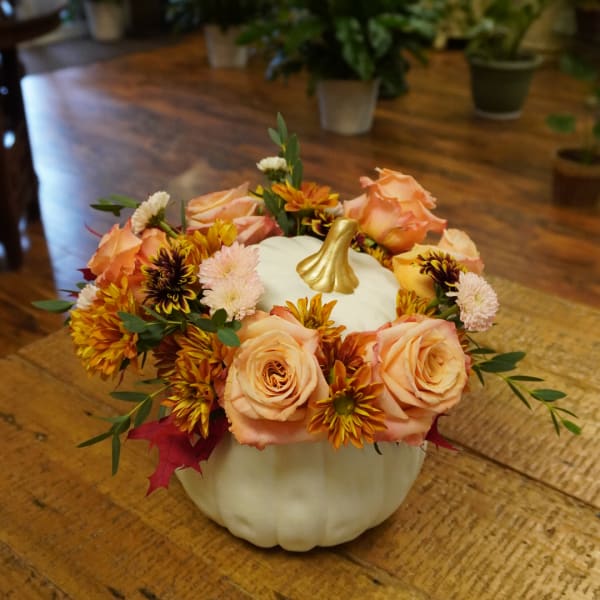 Floral arrangement in a white pumpkin container with peach roses and chrysanthemums