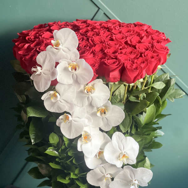 Heart-shaped red rose arrangement with cascading white orchids in a white vase