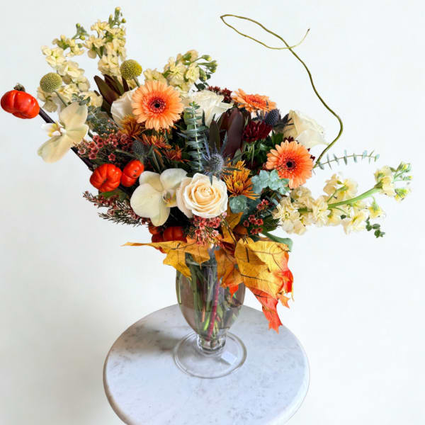 Autumn bouquet with orange gerberas, white roses, and cream orchids in a glass vase
