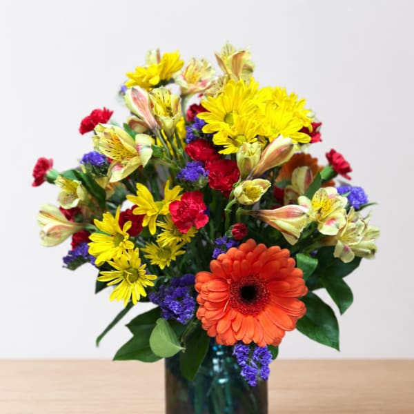 Mixed bouquet in a blue glass vase with orange, yellow, red, and purple flowers