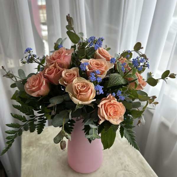 Peach roses and blue filler flowers in a pink vase