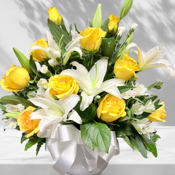 Yellow roses and white lilies in a white vase with a ribbon