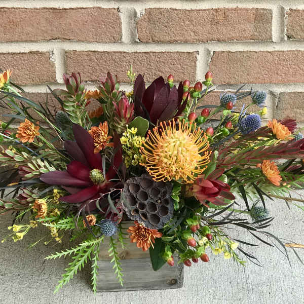 Mixed floral arrangement in a wooden box with orange and burgundy blooms