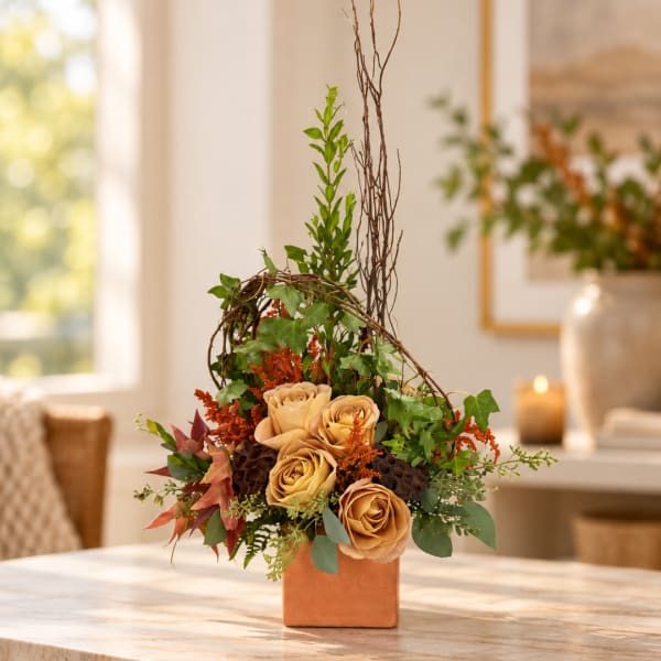 Tan roses in a square vase with ivy and twigs