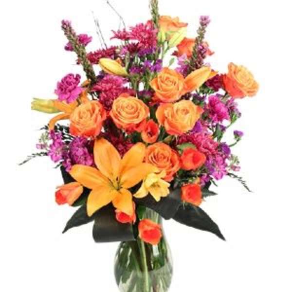 Orange roses and lilies in a glass vase with purple accents