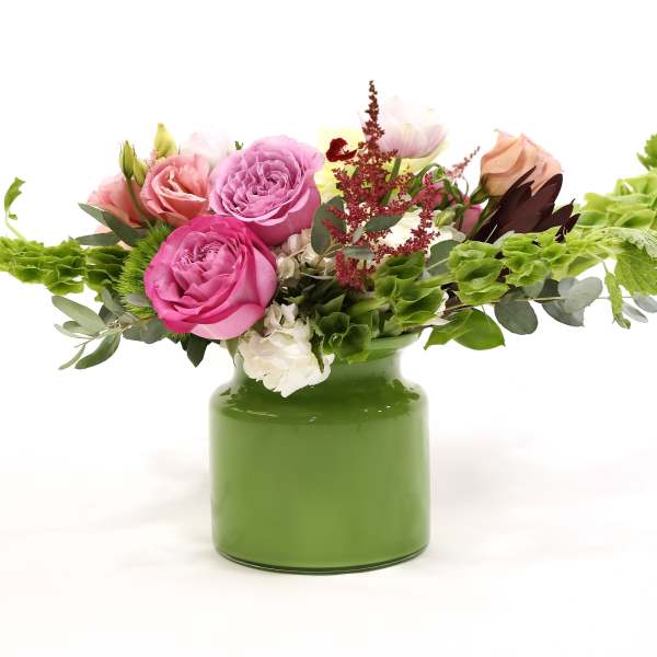 Pink and peach roses in a green vase with trailing greenery