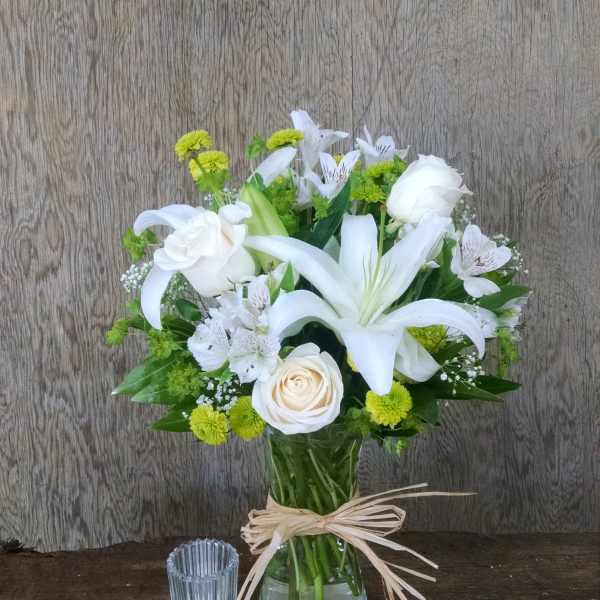 White lilies and roses in a glass vase with green accents