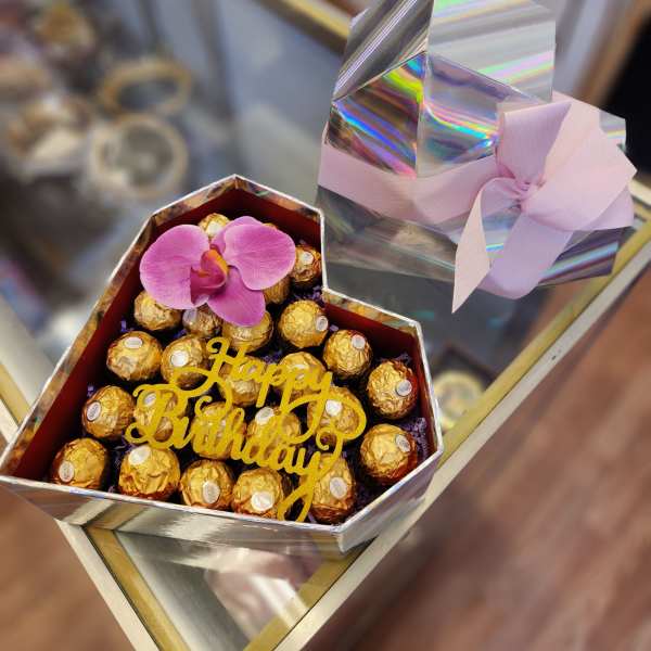 Gift box of chocolates topped with a pink orchid and birthday sign