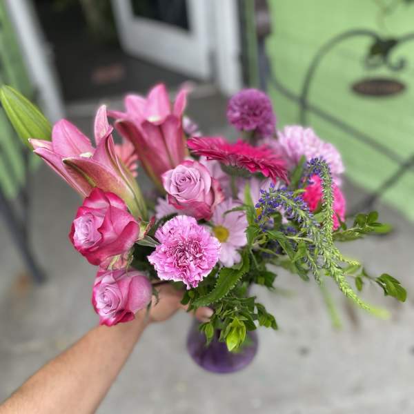 Handheld bouquet of pink roses, lilies, and mixed blooms in a purple vase