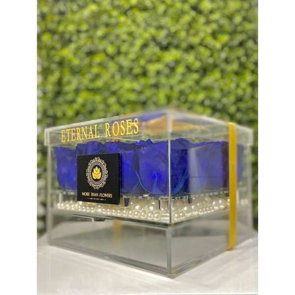 Acrylic box of vivid blue roses with white pearls at the base and gold lettering on the lid.
