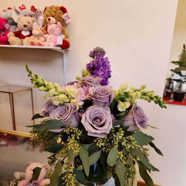 Lavender roses and purple flowers arranged in a glass vase