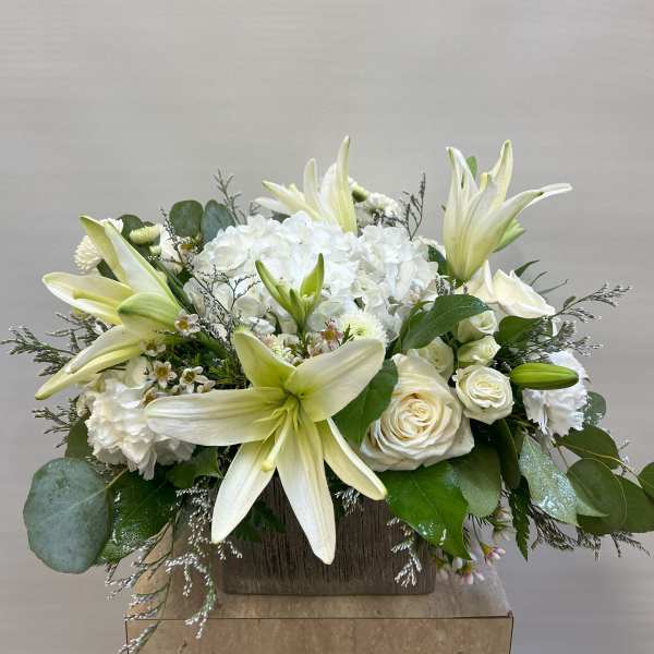 White lilies and roses arranged in a wooden box with greenery