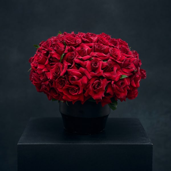 Red rose bouquet in a black vase on a dark pedestal