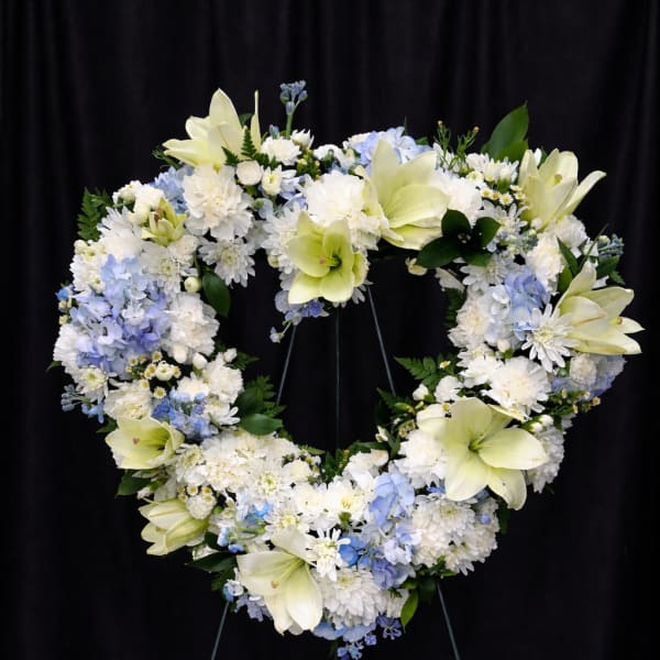 Heart-shaped floral wreath with white and pale blue flowers on a stand