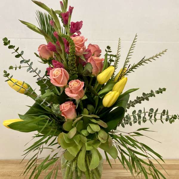 Pink roses and yellow tulips in a glass vase with greenery