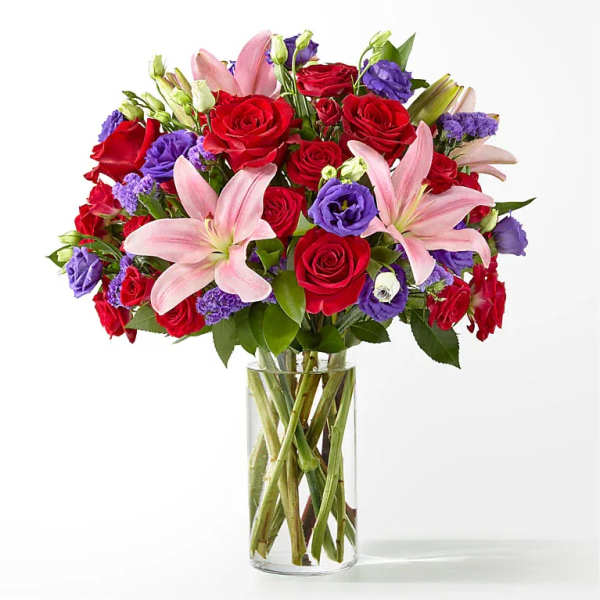 Bouquet of red roses, pink lilies, and purple flowers in a clear glass vase