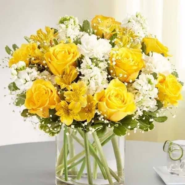 Yellow roses and white flowers arranged in a clear glass vase
