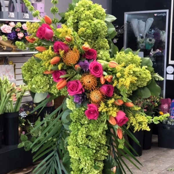 Tall cross-shaped standing spray with green hydrangeas, hot pink roses, and orange blooms on a metal easel