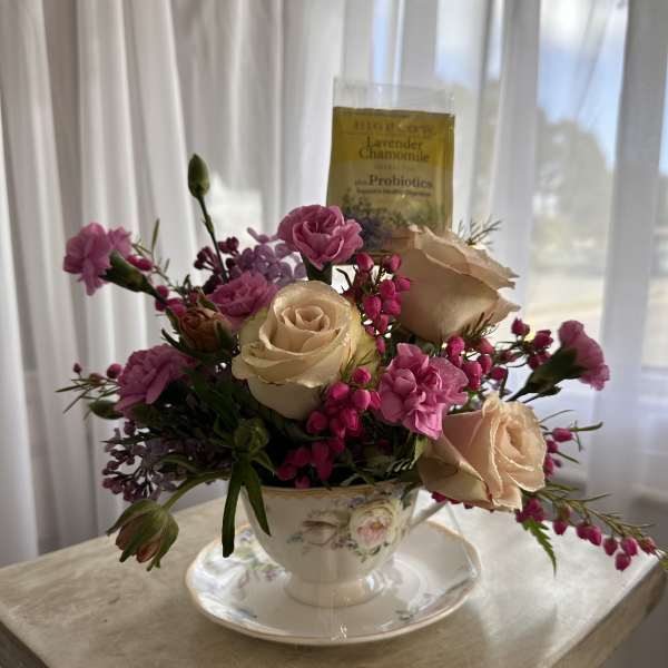 Pink and cream roses arranged in a teacup with a tea packet behind them.