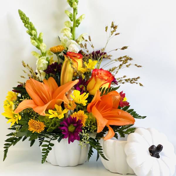 Orange lilies and mixed flowers in white pumpkin containers